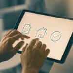 Mains interagissant avec une tablette affichant des icônes de document, maison et coche. Symbolise la gestion client numérique.