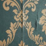 Gros plan sur du papier peint intissé vert sarcelle à motifs damassés dorés, montrant un raccord de lé et un pli.